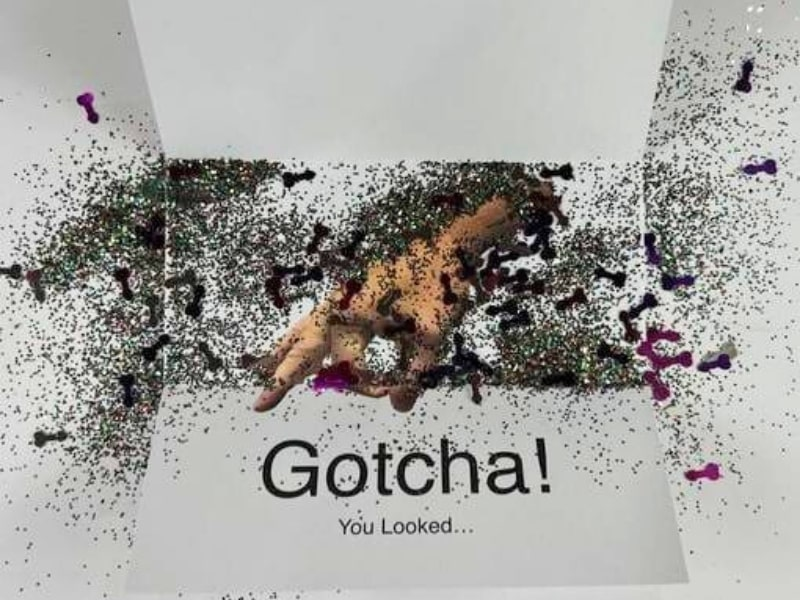 Funny Gotcha hand prank letter bursting with glitter confetti.