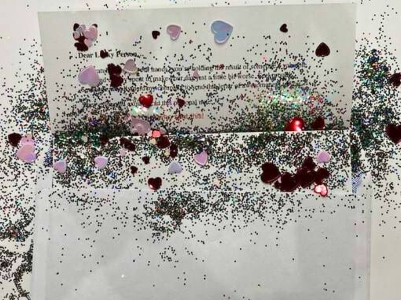 Secret admirer prank letter with heart confetti and glitter spilling from an envelope.